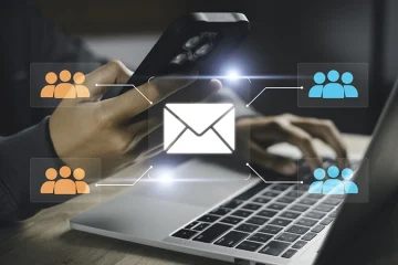 Person typing on a laptop and smartphone with a central inbox icon connected to orange and blue group icons, illustrating email distribution to groups.